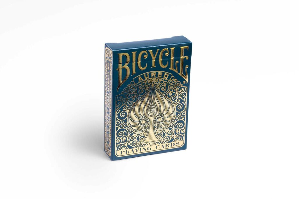 Eine Bicycle Creatives Aureo Kartenschachtel steht mit sichtbarer Vorderseite vor einem weißem Hintergrund.