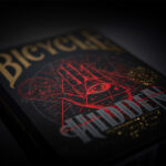 Eine Bicycle Creatives Hidden Kartenschachtel liegt angeschnitten sichtbar vor einem dunklen Hintergrund. Die Illustration der Vorderseite ist fokussiert.