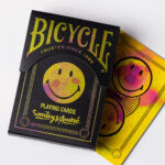 Die Bicycle Creatives Smiley André Kartenschachtel mit sichtbarer Vorderseite und eine Karte mit sichtbarem Backdesign liegen auf einem weißem Untergrund.