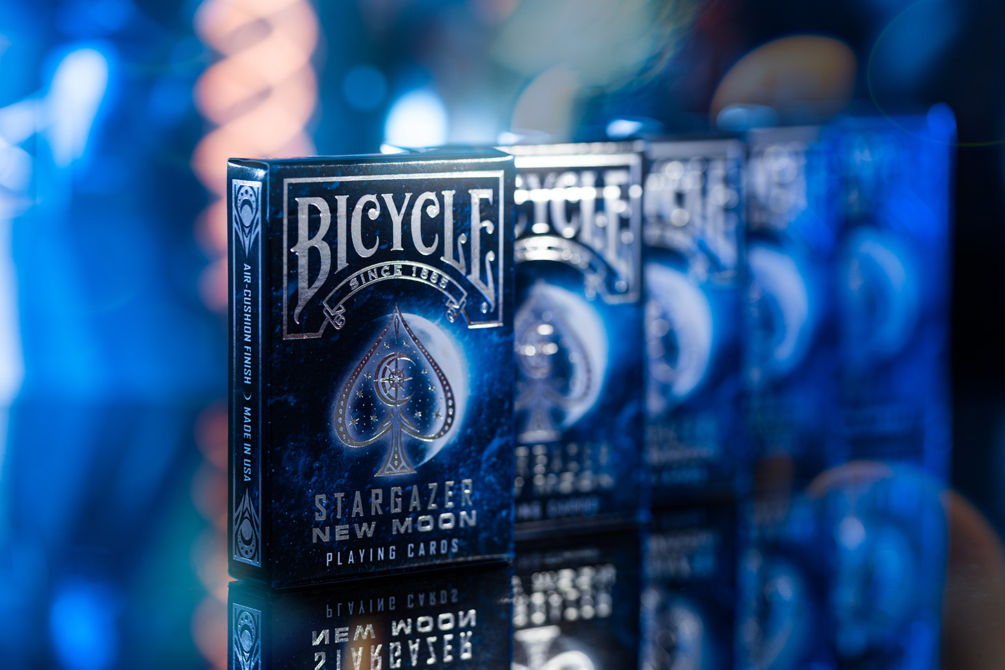 Fünf Bicycle Creatives Stargazer New Moon Kartenschachteln stehen mit sichtbaren Vorderseiten aufgereiht voreinander. Der Hintergrund ist blau, unscharf und atmosphärisch.