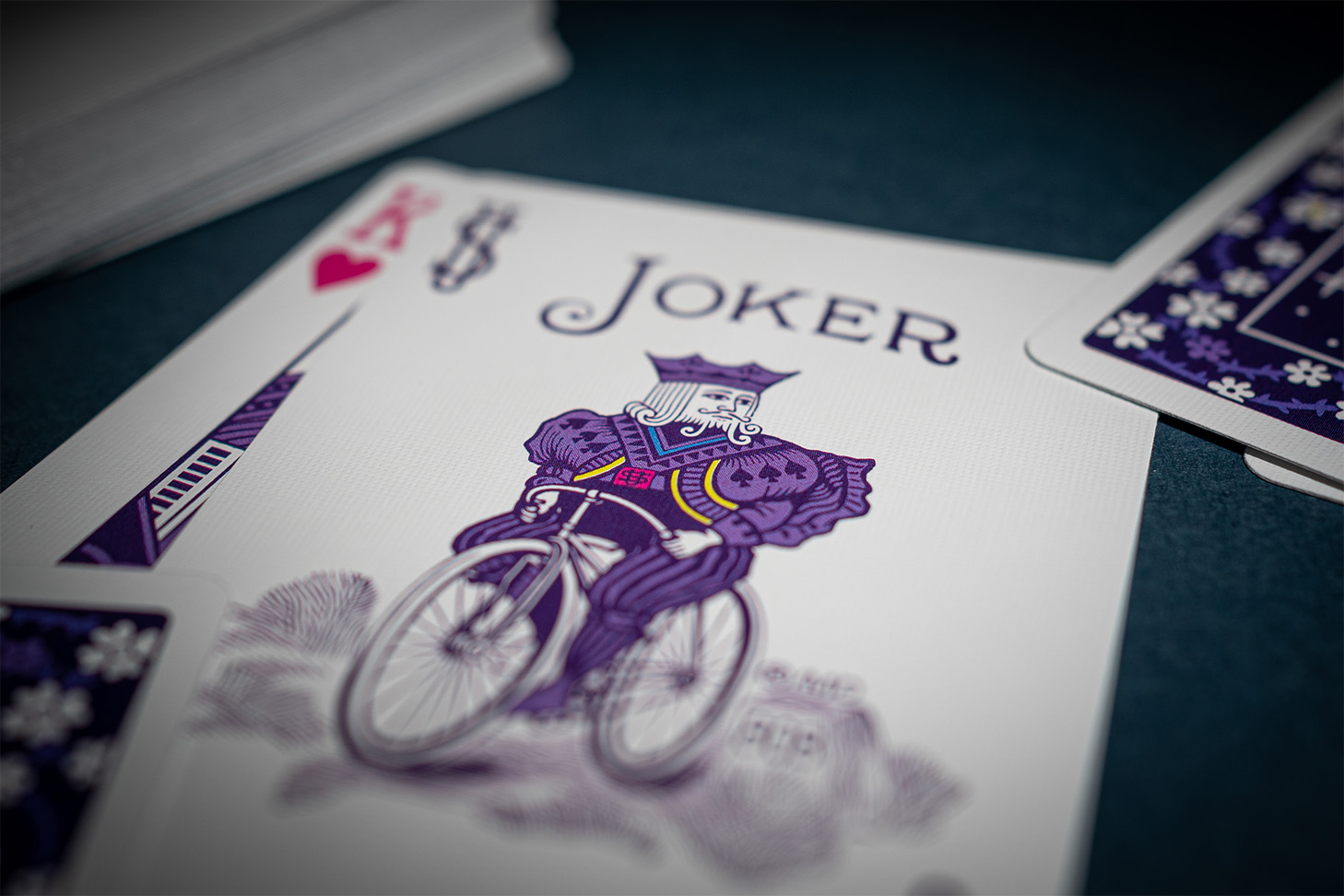 Die Bicycle Creatives Unicorn Karten Herz König und Joker liegen angeschnitten sichtbar auf einem dunklem Hintergrund. Daneben liegt ein Kartenstapel mit sichtbarem Backdesign.