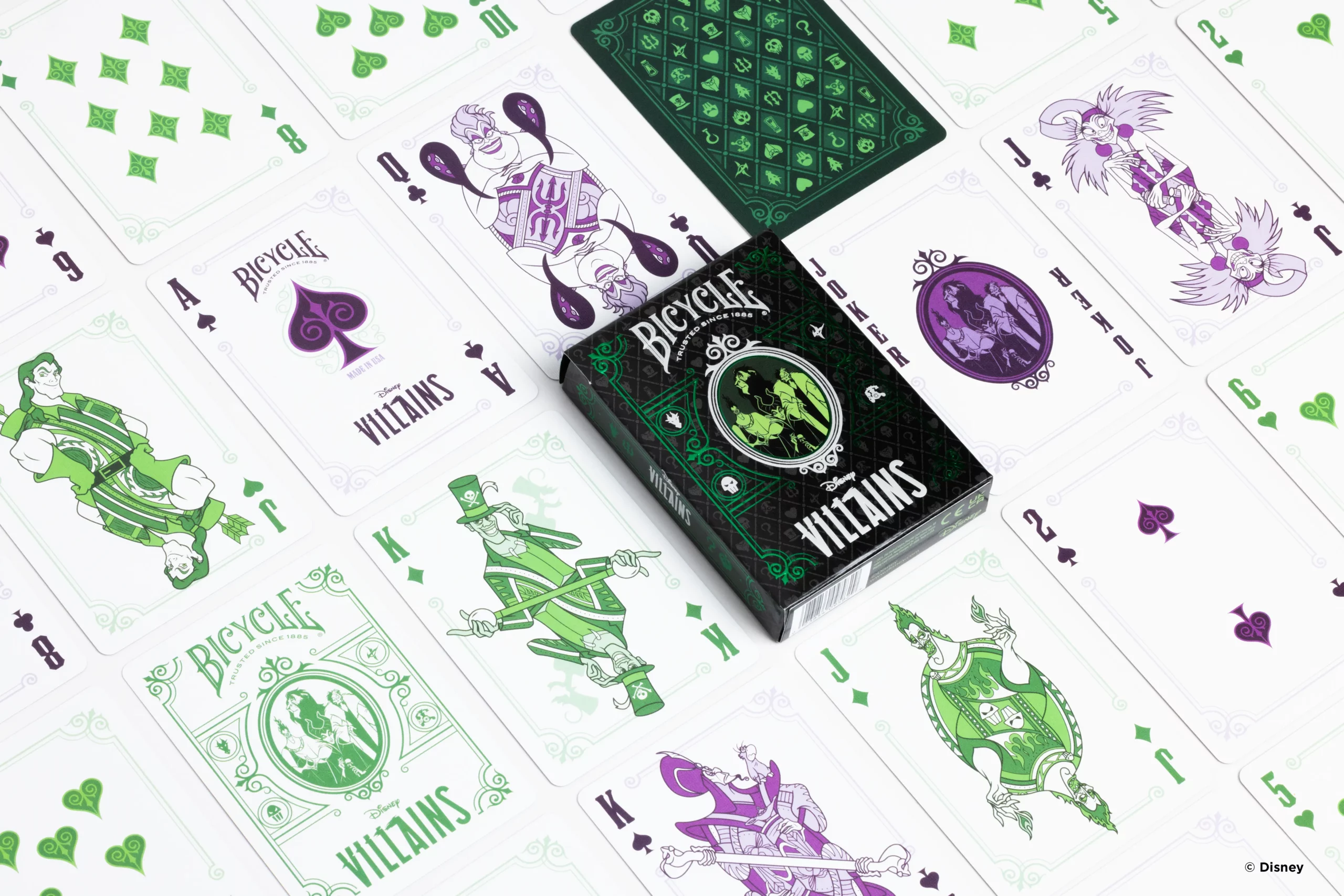 Die Karten einer Bicycle Creatives Bicycle Disney Villains green grün Kartenschachtel liegen ausgebreitet auf einer Fläche sodass man verschieden Vorderseiten und Rückseiten und die Schachtel sehen kann.