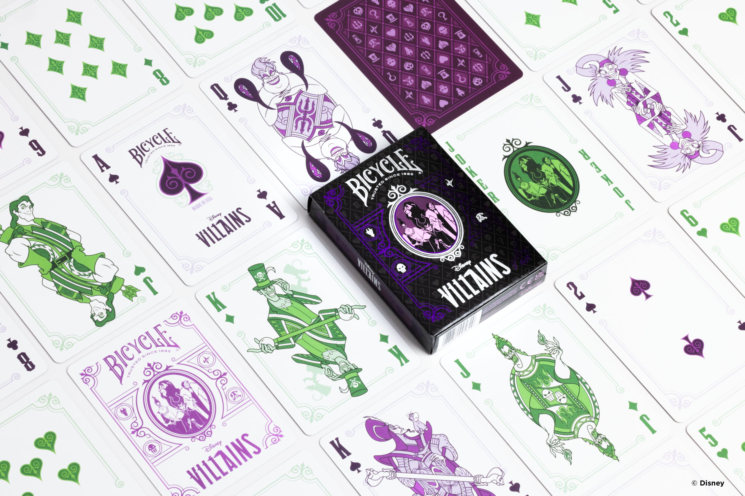 Die Karten einer Bicycle Creatives Bicycle Disney Villains purple lila Kartenschachtel liegen ausgebreitet auf einer Fläche sodass man verschieden Vorderseiten und Rückseiten und die Schachtel sehen kann.