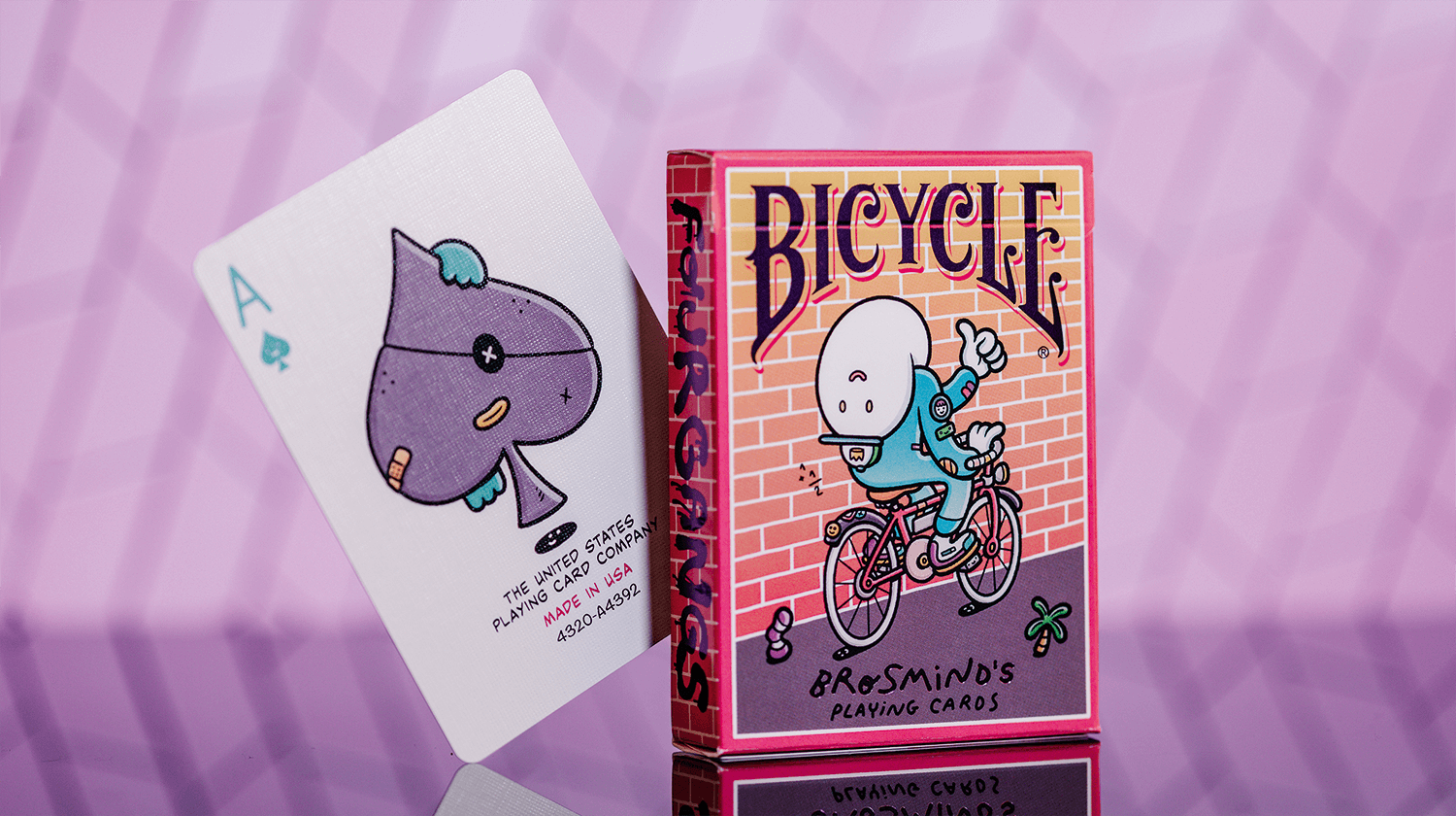 Eine Bicycle Creatives Brosmind Four Gangs Kartenschachtel steht mit sichtbarer Rückseite vor einem violetten Hintergrund aus Backstein, neben der Schachtel schaut eine Karte aus dem Deck hervor.