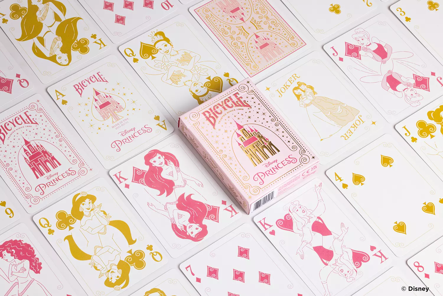 Die Karten einer Bicycle Ultimate Bicycle Disney Princess pink rosa Kartenschachtel liegen ausgebreitet auf einer Fläche sodass man verschieden Vorderseiten und Rückseiten und die Schachtel sehen kann.