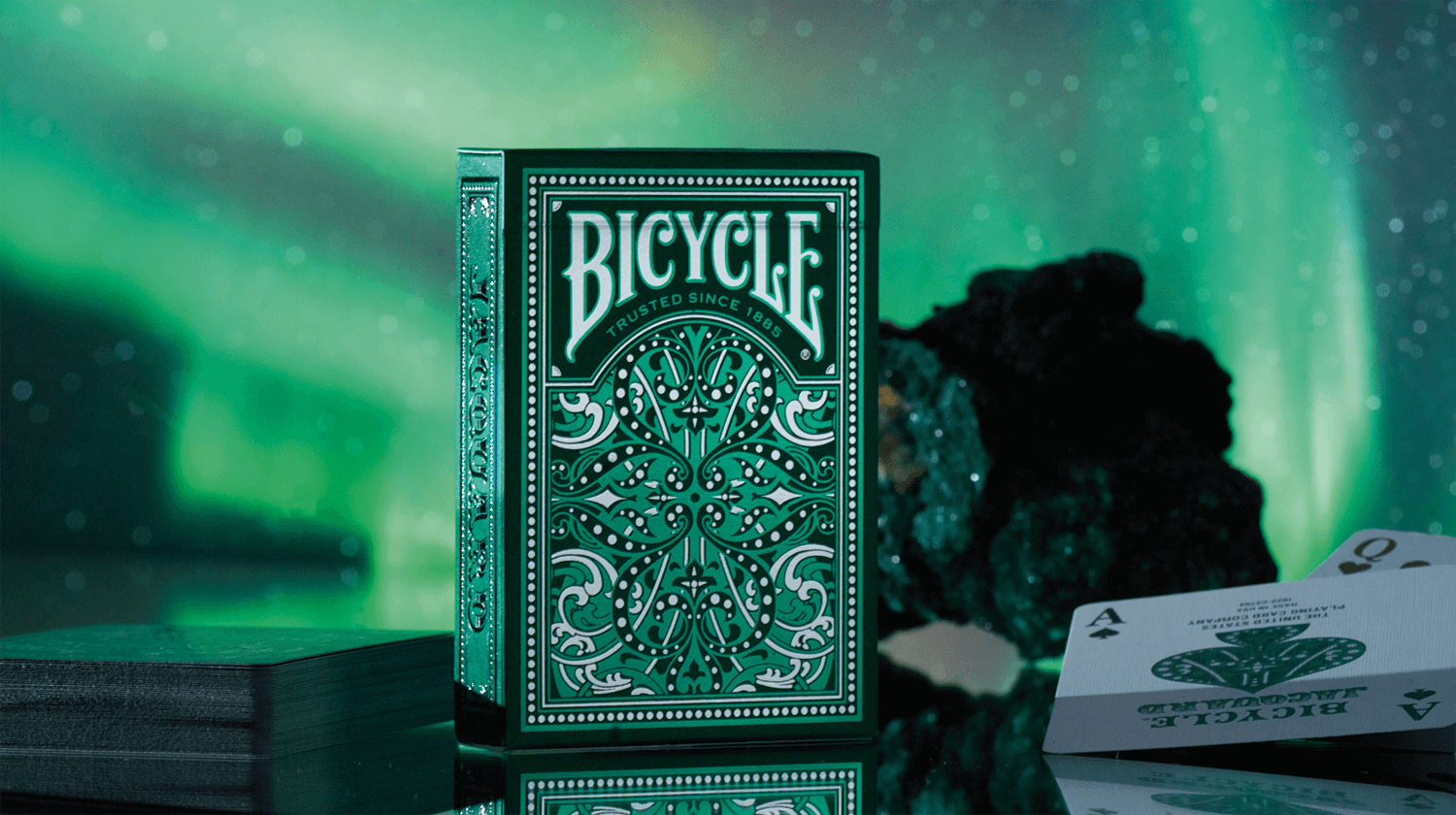 Eine Bicycle Creatives Jacquard Kartenschachtel steht mit sichtbarer Vorderseite vor einem grünen Hintergrund.