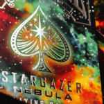 Zusehen ist eine Bicycle Creatives Kartenschachtel von Stargazer Nebula in einer nahen Ansicht in der man die Veredelung mit Folie erkennen kann, im Hintergrund sieht man die Rückseiten der Karten.