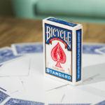Eine Bicycle Trick Deck Blank Face Blue Blau Kartenschachtel steht auf einem Tisch, unter der Schachtel sind Karten ausgebreitet. Die Karten haben nur eine blaue Rückseite, die Vorderseite ist leer.