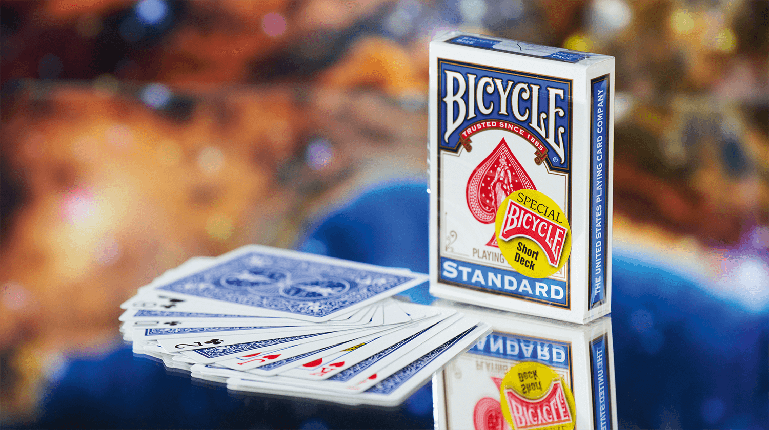 Eine Bicycle Trick Deck Short Deck Blau Blue Kartenschachtel auf einem Tisch, davor liegen aufgefächert einige Karten.