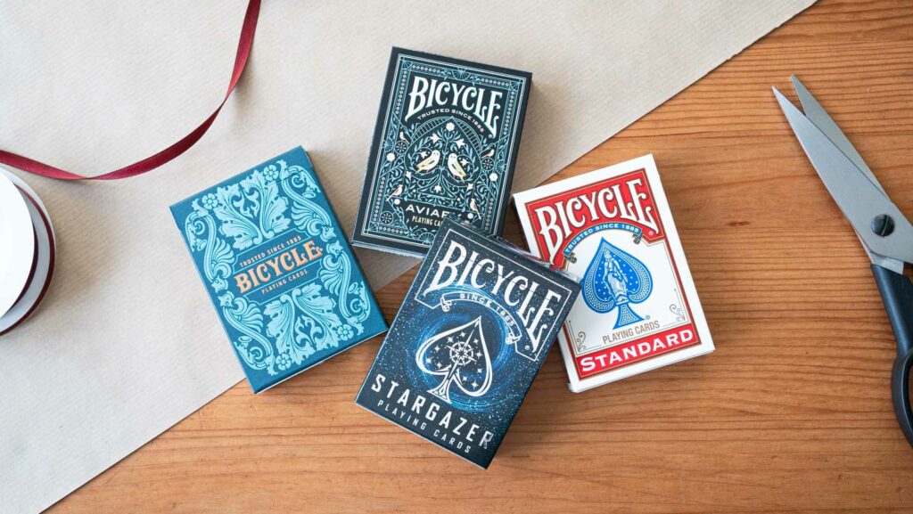 Bicycle Sea King, Original, Stargazer, und Aviary  Kartendeck auf- Holztisch als Geschenk mit Schleife. Kleine günstige Geschenke – Bicycle – Spielkarten.