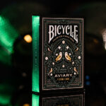 Eine Bicycle Creatives Aviary Kartenschachtel steht mit sichtbarer Vorderseite vor einem dunklem und unscharfem Hintergrund.