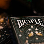 Zwei Bicycle Creatives Aviary Kartenschachteln liegen mit jeweils sichtbarer Vorder und Rückseite übereinander vor einem dunklem Hintergrund.
