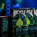 Vier Bicycle Creatives Dark Mode Kartenschachteln stehen hintereinander. Die Vorderseite der ersten Schachtel ist sichtbar. Daneben steht ein Kartenstapel mit sichtbarem Backdesign. Der Hintergrund ist unscharf.