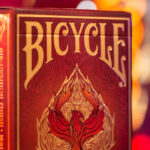 Eine Bicycle Creatives Fyrebird Kartenschachtel steht mit sichtbarer Vorderseite vor einem unscharfem Hintergrund. Das Bicycle Logo und die Fyrebird Illustration sind sichtbar.