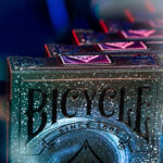 Mehrere Bicycle Creatives Stargazer Kartenschachteln stehen hintereinander vor einem unscharfem, dunklem Hintergrund. Die Vorderseite der ersten Schachtel ist angeschnitten sichtbar und zeigt das Bicycle Logo.