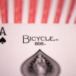 Die Pik Ass Bicycle Originals Gold Standard Rot Karte liegt auf einem Kartenstapel mit sichtbaren Rückseiten.