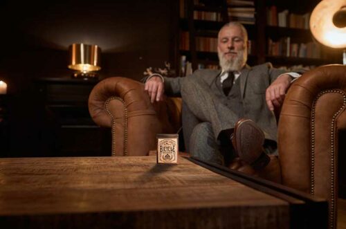 Gentleman sitzt in Ledersessel und vor ihm auf einem Holztisch steht das Kartenspiel Bicycle® Bourbon. Whisky-Geschenke für Männer, Bicycle Spielkarten