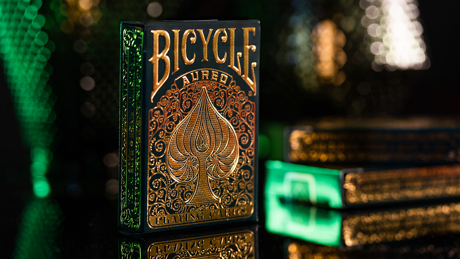 Die Aufnahme zeigt das Bicycle Creatives Aureo Kartendeck mit sichtbarer Vorderseite welches mit Goldfolie veredelt ist und glänzt. Der Hintergrund ist atmosphärisch und unscharf.