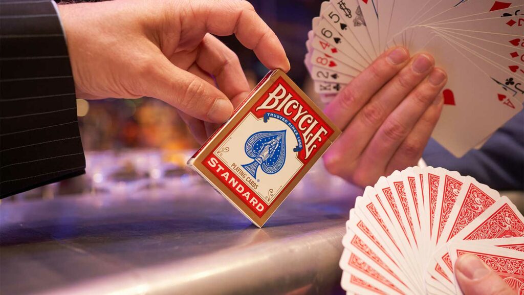 Hand hält Kartenschachtel mit Bicycle Originals, daneben zwei Kartenfächer. Zaubershow, Zaubershows, die große Zaubershow, Bicycle Spielkarten