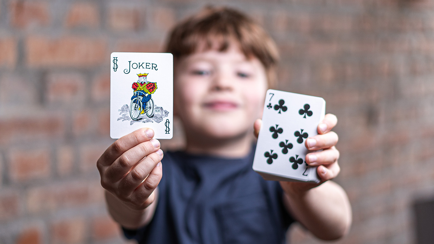 Ein Junge führt stolz einen Zaubertrick vor und zeigt die Bicycle Joker Karte hoch.