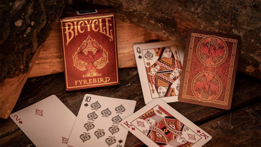 Kartendeck Fyrebird mit einzelnen Karten und Verpackung vor Holzstapel. Element Feuer, Bicycle Spielkarten.