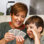 Eine Mutter hält Karten in der Hand und erklärt ihrem Sohn ein Spiel. Sie weiß was richtig ist für ihr Kind – Spielen.