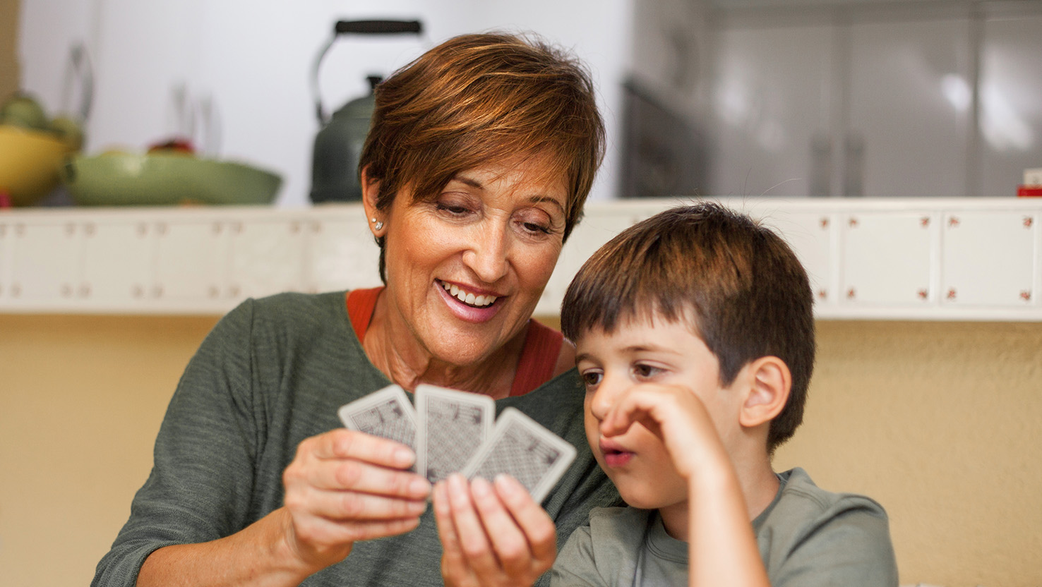 Eine Mutter hält Karten in der Hand und erklärt ihrem Sohn ein Spiel. Sie weiß was richtig ist für ihr Kind – Spielen.