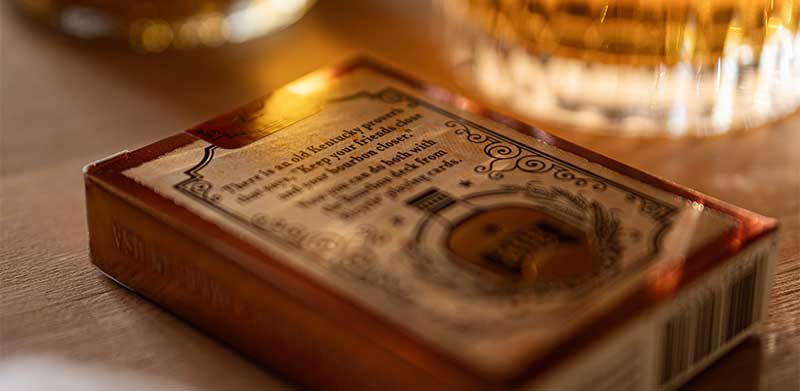 Nahaufnahme der Rückseite des Kartenspiel Bicycle® Bourbon mit Fokus auf einem Text über das Bild. Im Hintergrund eine Whisky-Falsche mit Glas. Whisky-Geschenke für Männer, Bicycle Spielkarten