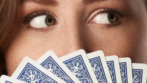 Nahaufnahme eines Gesichts einer Frau: Augen schauen über Kartenfächer nach rechts. Spielkarten Design. Bicycle Spielkarten