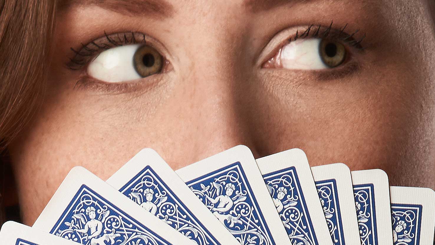 Die Nahaufnahme zeigt das Gesicht einer Frau: Die Augen schauen über den Kartenfächer nach rechts.