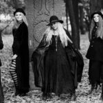 Schwarz-Weiß-Foto von fünf schwarz gekleideten Frauen, die Gothic Look tragen, und im Wald in Laub stehen.