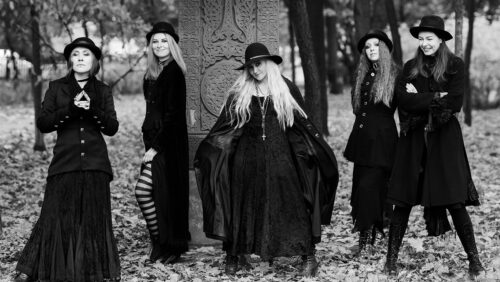Schwarz-Weiß-Foto von fünf schwarz gekleideten Frauen, die Gothic Look tragen, und im Wald in Laub stehen.