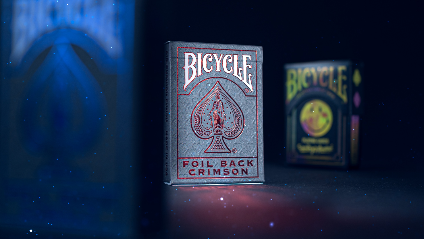 Die Bicycle Ultimate Foil Back Crimson Red und das Bicycle André Kartendeck stehen vor einem dunklem und unscharfem Hintergrund.